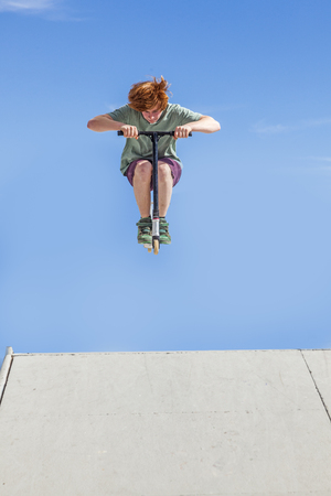 boy with scooter is jumping at the skate parkの写真素材