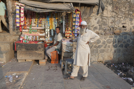 NEW DELHI, INDIA - NOV 17, 2011: senior man stands in front of a kiosk at the Meena Bazaar area in Old Delhi while the owner of the kiosk relaxes in the midday heat.のeditorial素材