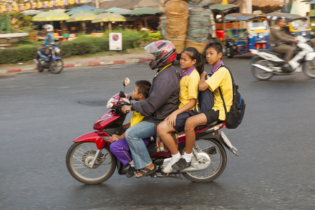 BANGKOK, THAILAND - JAN 4, 2010: man with motor bike gives his children a lift to school in early morning. Pupils wear school uniforms.のeditorial素材