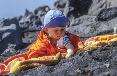 cute young baby enjoys exploring the black sand at the beach in Lanzaroteの写真素材