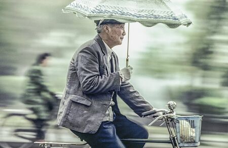 Beijing, China - August 1, 1982: old man rides his bicycle with umbrella in his arm. I 1982 bicycle was for more than 95 percent of chinese people the way for transportation even in Beijing.のeditorial素材
