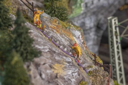 plastic exausted walker climbing up a steep rock of the scenic model landscapeの写真素材