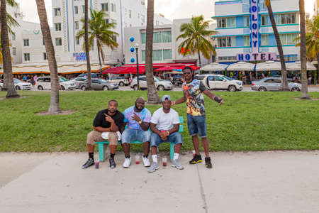 Miami, USA - August 30, 2014: black people posing and sitting at a bench at ocean drive with colony hotel in background.のeditorial素材