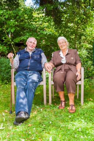 elderly happy couple sitting hand in hand in their gardenの写真素材