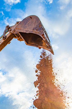 detail of excavator bucket filled with soil under blue sky