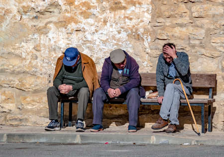 Valencia, Spain - January 9, 2019: three senior men sitting on a bench an looking sadly at the floor.のeditorial素材