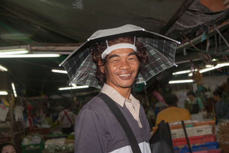 Bangkok, Thailand - May 12, 2009: unidentified man wears a funny cap made of an umbrella at the morning flower market Pak Klong Thalat.のeditorial素材