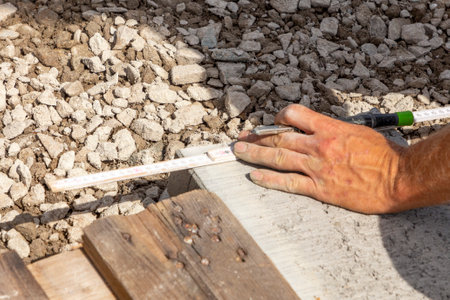 Drawing a straight line with a pencil on a concrete curb. Marking guidelines for cutting. Hands of a...
