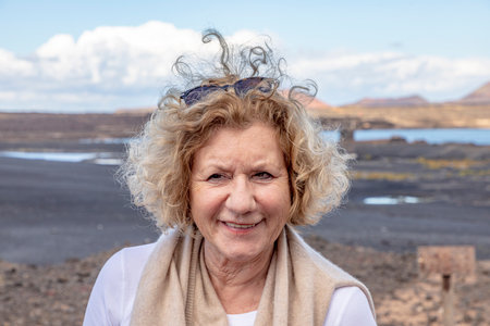 portrait of attractive elderly woman in nature with wind in hair and volcanic landscape in...