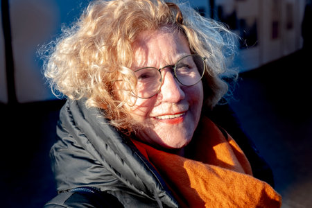 portrait of attractive positive looking elderly caucasian woman in winter time with scarf and glassesの写真素材