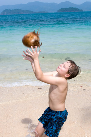 boy is playing with a coconut on a beautiful beach in Thailandの写真素材
