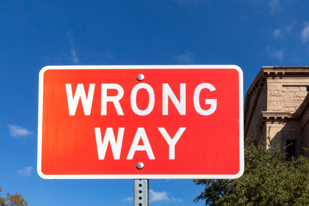 warning sign wrong way on red background under blue skyの写真素材