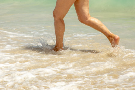 feet of attractive mature woman running on the beach in the water in detailの写真素材