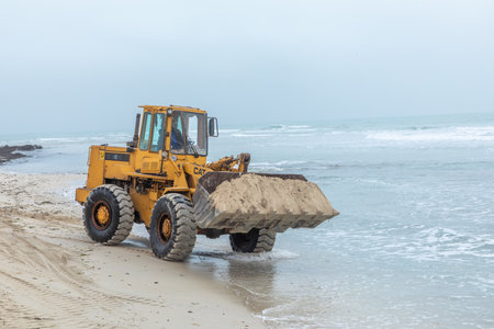 Djerba, Tunisia - April 29, 2024: The shovel crane transports sand at the beach to guarantee a fine...