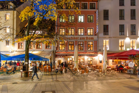 Munich, Germany - November 17, 2024: People enjoy the evening at the Marienplatz sitting by night at the Augustiner am Dom bar and drinking beer.のeditorial素材