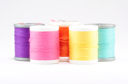 Five spools of sewing thread, arranged from left to right purple, pink, orange, yellow, light blue の写真素材