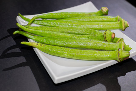 Fresh okra on a white plate on a black background close upの写真素材