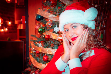Happy young woman in Santa hat near christmas tree at home.の写真素材