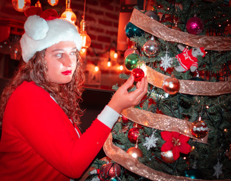 A young woman in a Santa hat decorates the Christmas tree.の写真素材