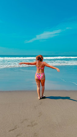 A young girl in a pink bikini is standing on the beach.の写真素材