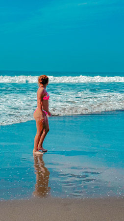 Young woman in pink swimsuit standing on the beach and looking at the seaの写真素材