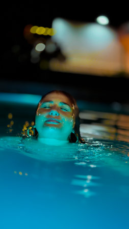 Portrait of a beautiful young woman relaxing in swimming pool at night