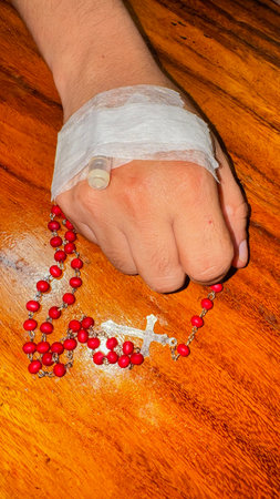 Closeup of a real patient's hand with intravenous infusion. (IV) holding a rosary. prayer concept...