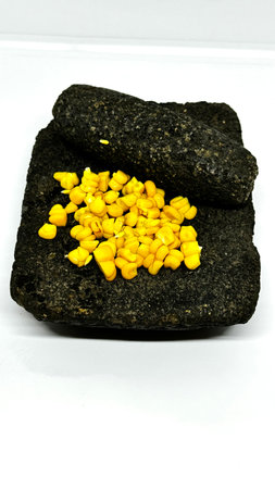 Metate with corn kernels on a white background. A traditional Mesoamerican grinding stone,...