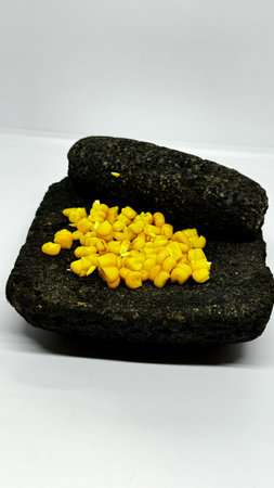 Metate with corn kernels on a white background. A traditional Mesoamerican grinding stone,...