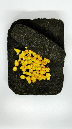 Metate with corn kernels on a white background. A traditional Mesoamerican grinding stone,...