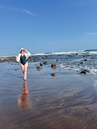 Young woman in a hat and a swimsuit walking on the beach