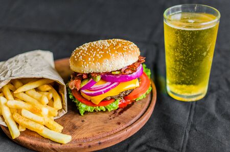 Burger and french fries on a wooden table against black backgroundの写真素材