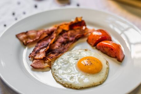 Fried chicken eggs with crispy bacon and tomatoes against white backgroundの写真素材