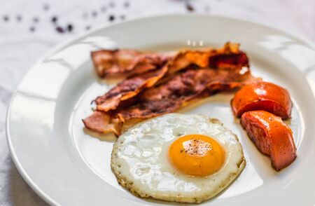 Fried chicken eggs with crispy bacon and tomatoes against white backgroundの写真素材