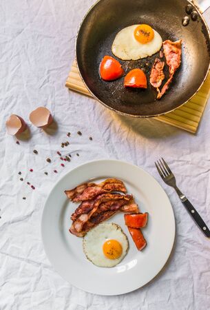 Fried chicken eggs with crispy bacon and tomatoes against white backgroundの写真素材