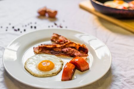 Fried chicken eggs with crispy bacon and tomatoes against white backgroundの写真素材