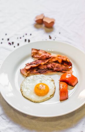 Fried chicken eggs with crispy bacon and tomatoes against white backgroundの写真素材