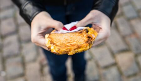Eating a sandwich with grilled melted cheese and bacon at a street food marketの写真素材