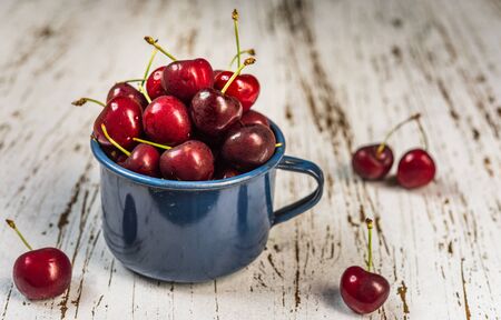 Cup with fresh colorful organic black cherries fruit against wooden background.の写真素材