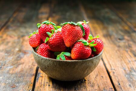 Bowl with fresh colorful organic strawberries fruit against wooden background.の写真素材