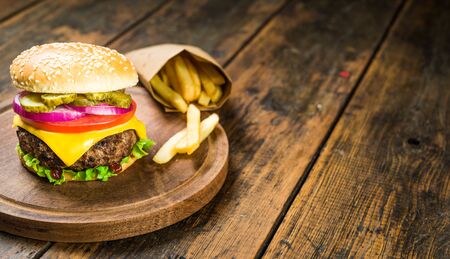 Cheese burger and french fries against wooden background. Tasty fast food.の写真素材