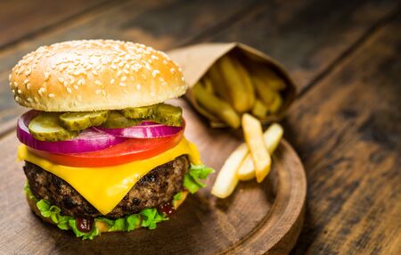 Cheese burger and french fries against wooden background. Tasty fast food.の写真素材