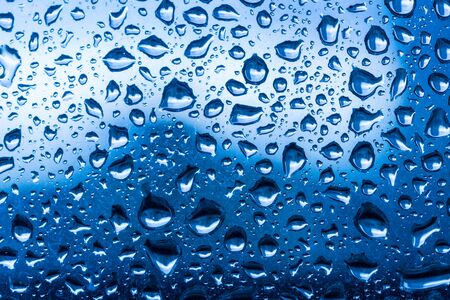 Water drops on glass window blue background after the rain in the autumn fall.の写真素材