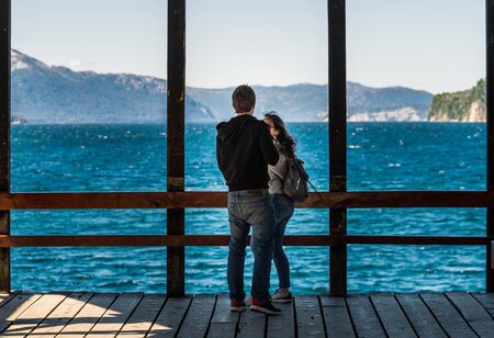 A couple in love standing on wooden pier at the lake with blue waterの写真素材