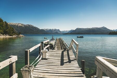 Landscape photo with old wooden pier, transparent lake water, and mountainsの写真素材