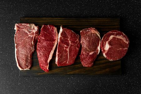 Selection of raw beef meat food steaks against black stone backgroundの写真素材