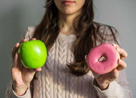 Woman holding a doughnut and green apple. Concept of healthy and unhealthy foodの写真素材