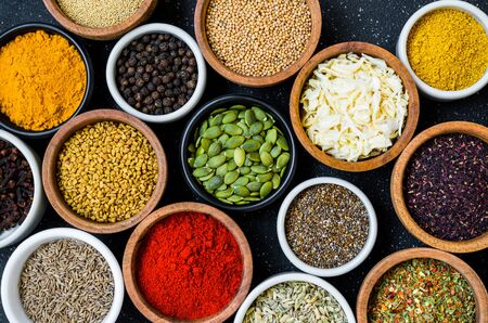 Variety of colorful spices, herbs, and seeds on black stone backgroundの写真素材