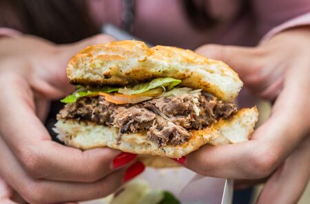 Young woman eating a duck meat burger at a street food marketの写真素材