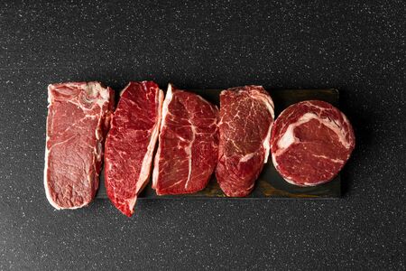 Selection of raw beef meat food steaks against black stone backgroundの写真素材